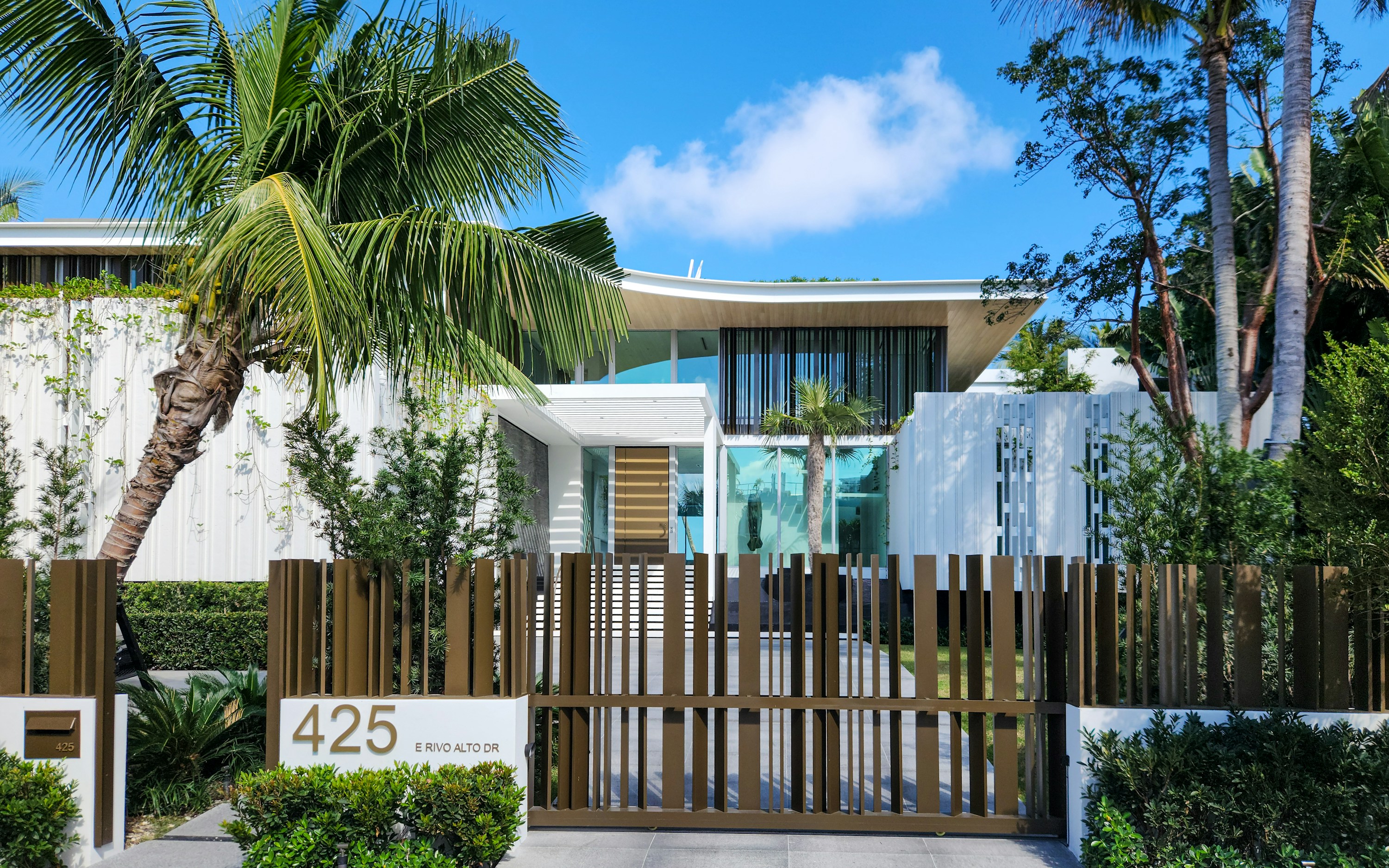 Modern white Miami Beach residence behind a bronze driveway gate and tropical palms